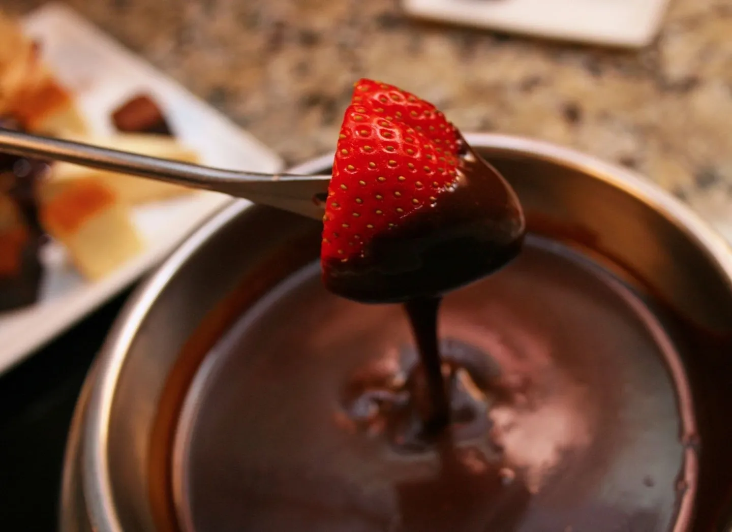 A spoon is being dipped into chocolate with strawberries.